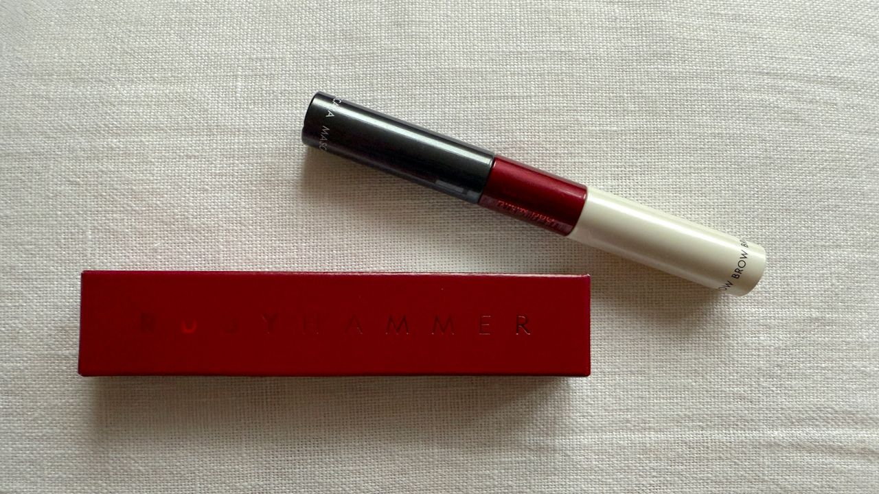 Image of the Ruby Hammer Mascara &amp; Brow Duo laying horizontally above its red box, set against a white linen background