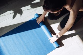 Overhead view of young Asian sports woman practicing yoga / exercising at home. Unrolling yoga mat, getting prepared to work out in the fresh bright morning