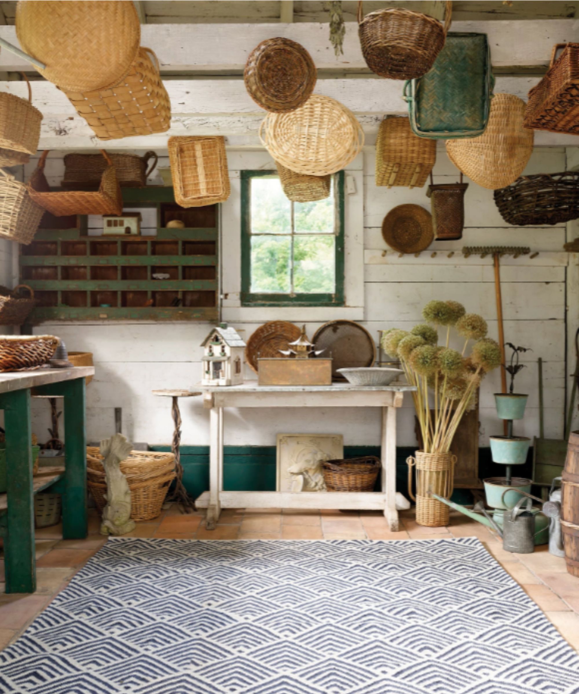 potting garden shed rustic white shiplapped walls, terracotta floor, baskets hung from the ceiling beams and a white and blue patterned rug on the floor