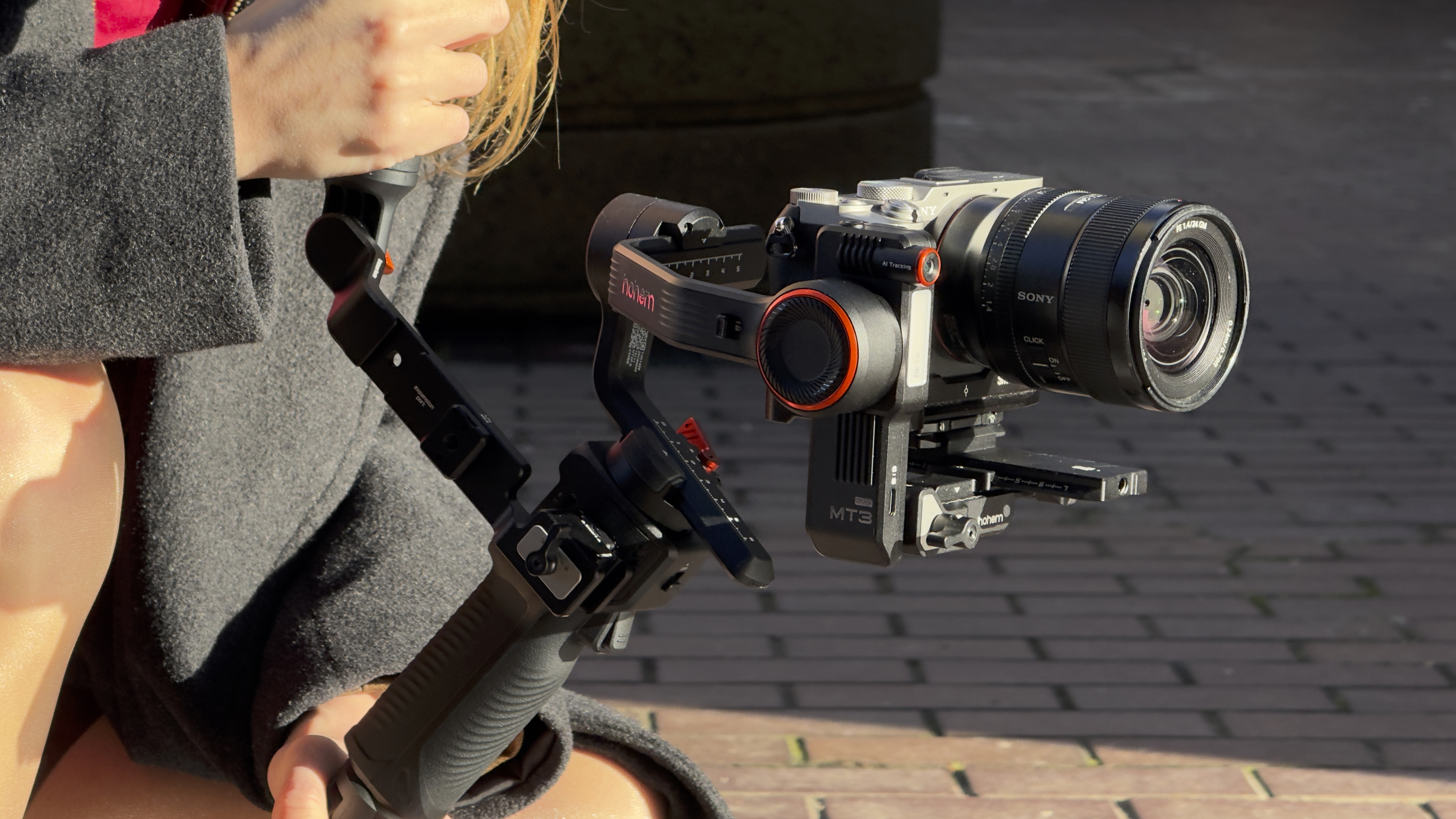 Close-up of a Sony mirrorless camera mounted on a Hohem MT3 3-axis gimbal, showing the AI tracking module attached beside the camera body.