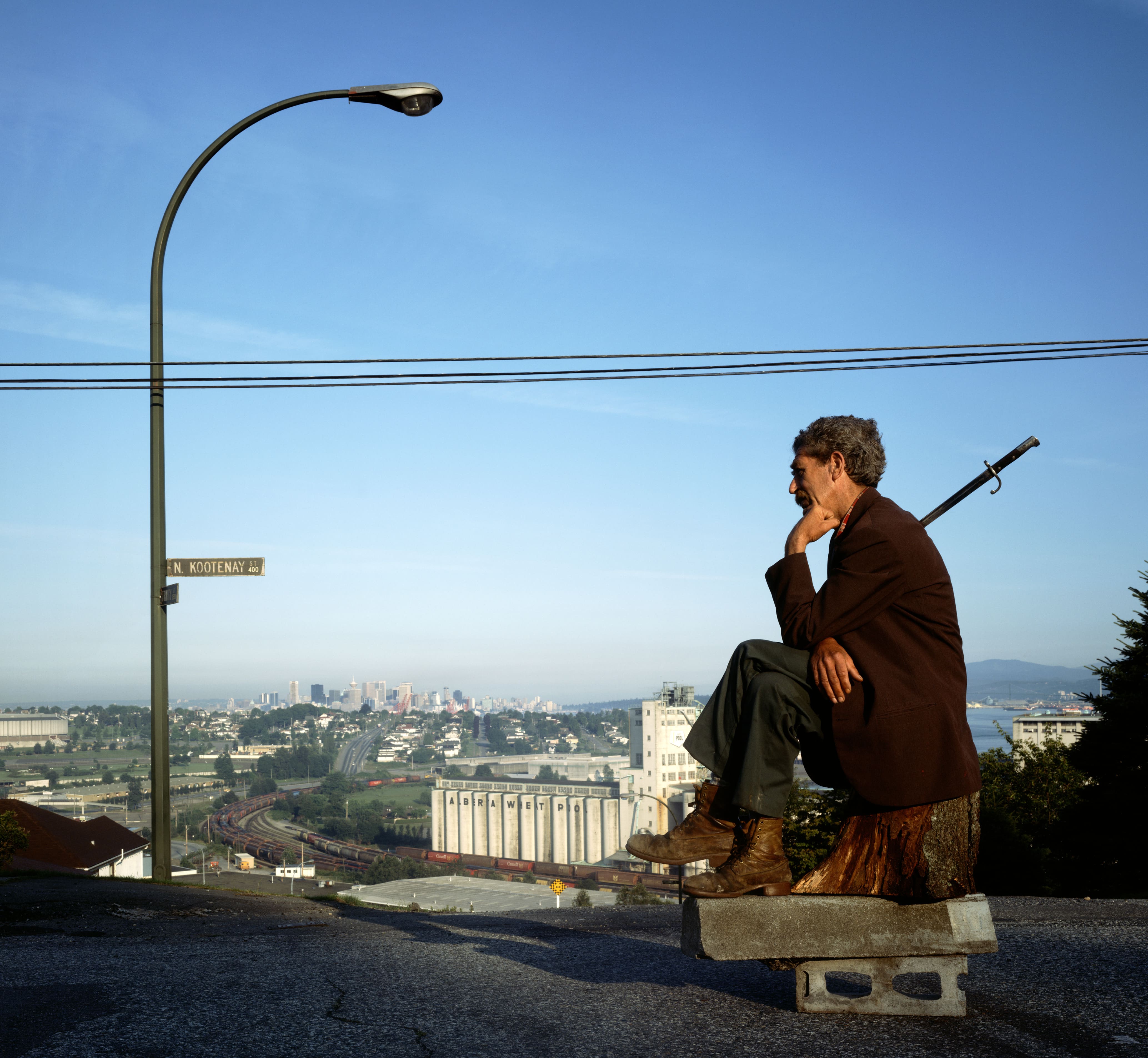 A man sits on a concrete block and tree stump, resembling Rodin's 