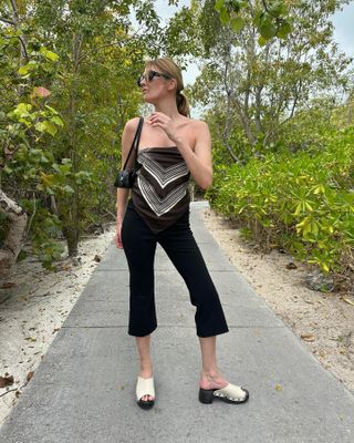 Woman wears black capri pants, a bandana tube top, Dr. Scholl's clog sandals and an Alaia Le Teckel bag.