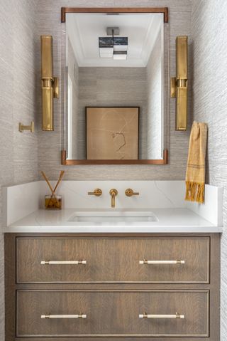 wooden bathroom vanity in small bathroom with marble countertop and gold wall lights