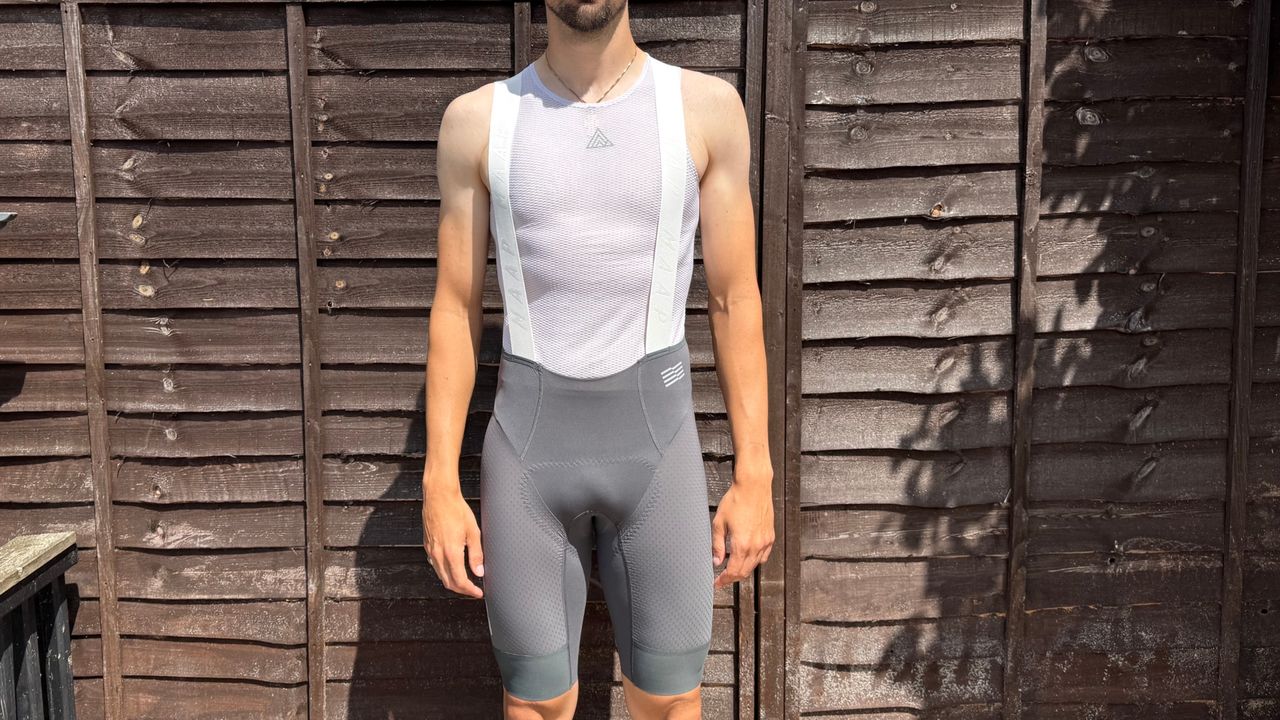 Andy Turner wares the grey MAAP Pro bib shorts 2.0 standing infront of a wooden fence 