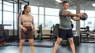 Man demonstrates medicine ball core rotation exercise as woman looks on