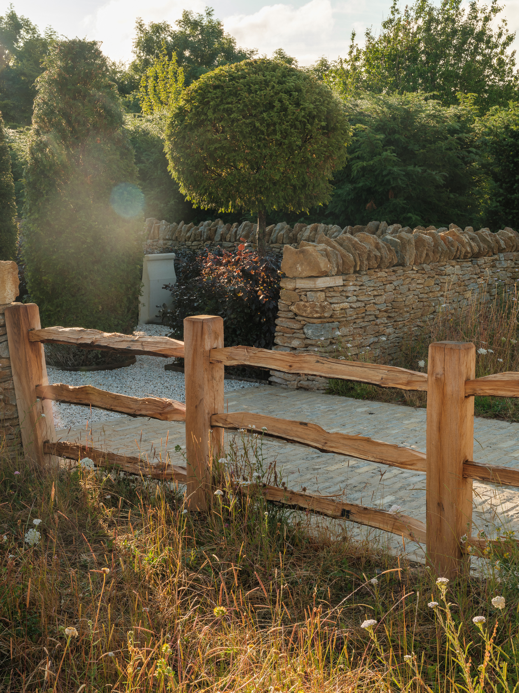 The Newt in Somerset garden with stone path, timber fence, wild plantings, stone fence and topiary