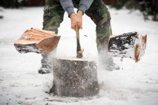 A lumberjack is splitting wood with an axe in snow.