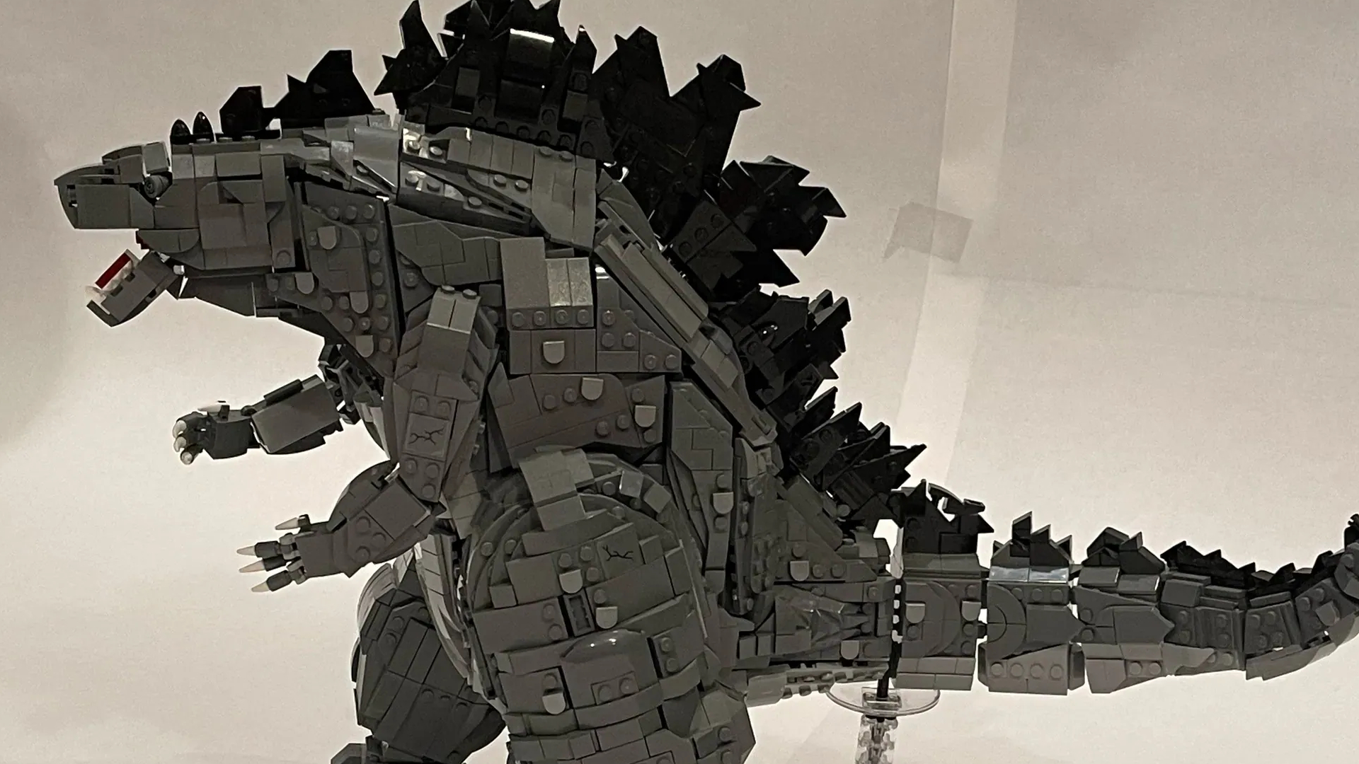 A Lego Godzilla model standing against a paper background, seen from the side