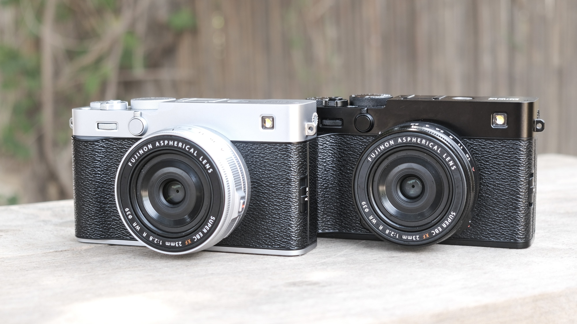 All black Fujifilm X-E5 alongside a silver Fujifilm X-E5, on a wooden bench