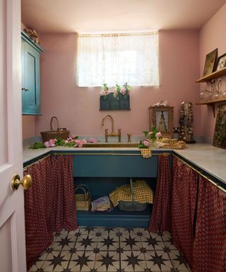 pink laundry room with white countertops, blue cabinets with cafe curtain and black and white tiled flooring