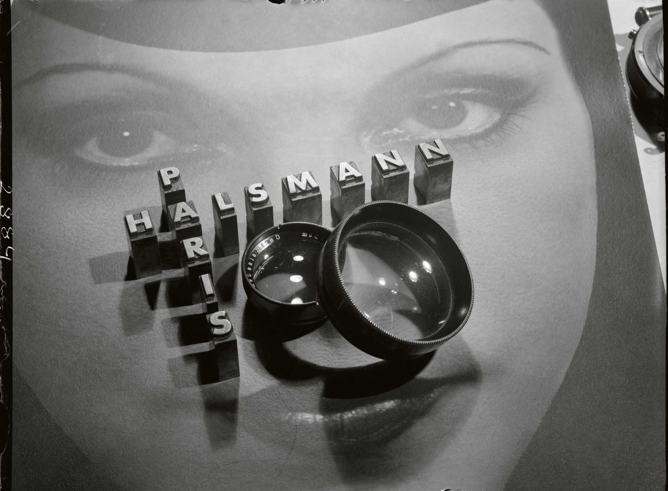 Metal letterpress blocks spelling "Halsmann Paris" rest on a photograph of an eye, alongside a camera lens.