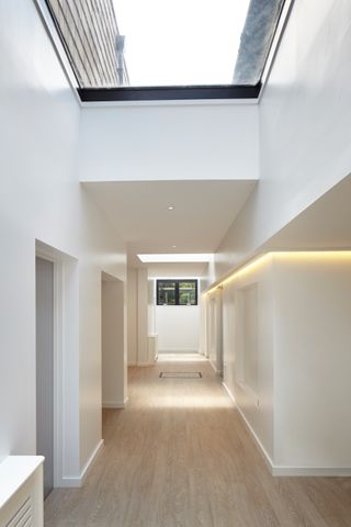 a wide, white open hallway, with feature glazing in the rooflights, shining light onto wooden floors