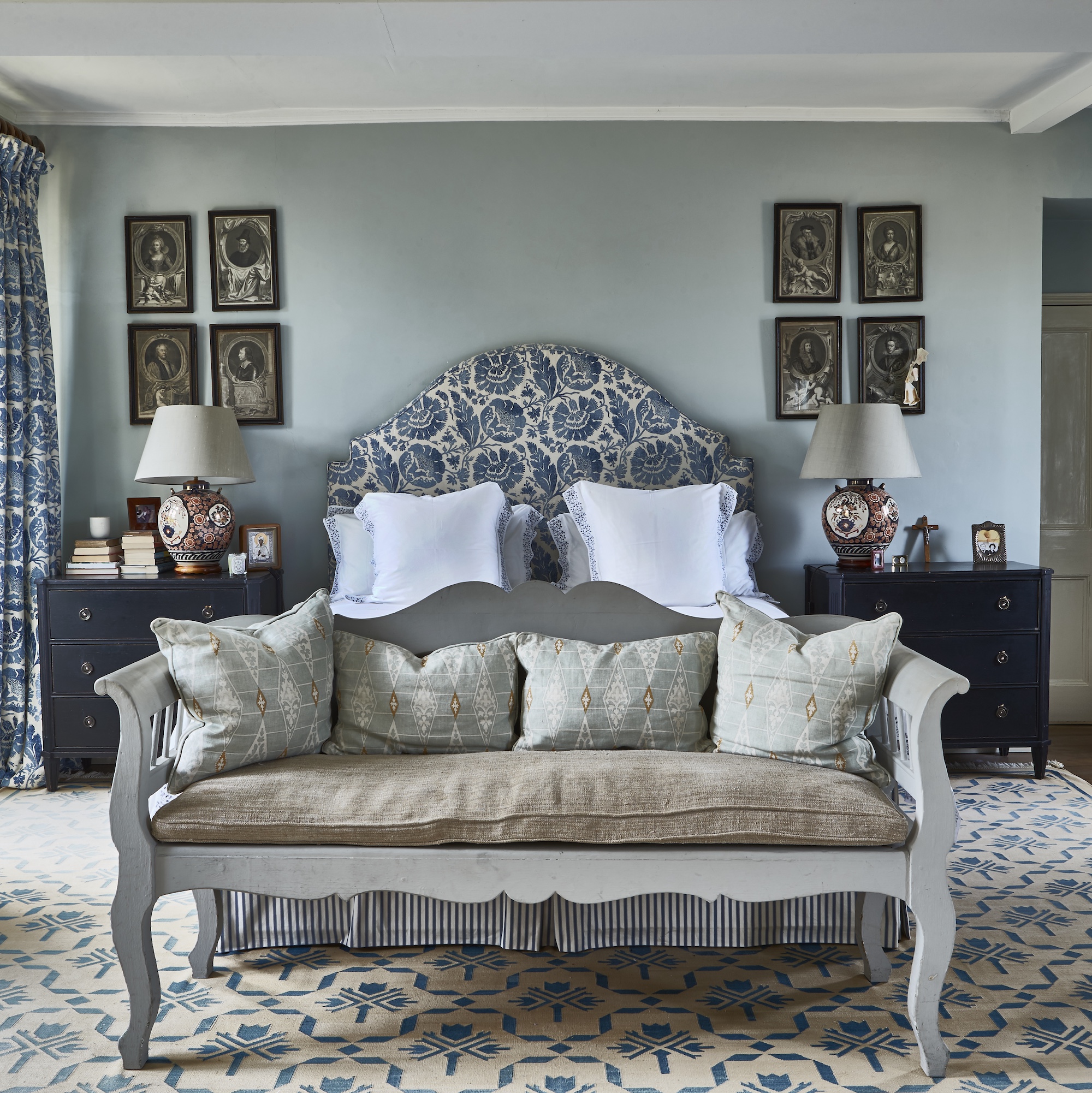 traditional english country house bedroom with pale blue walls, upholstered bed, bench seat and rug on floor