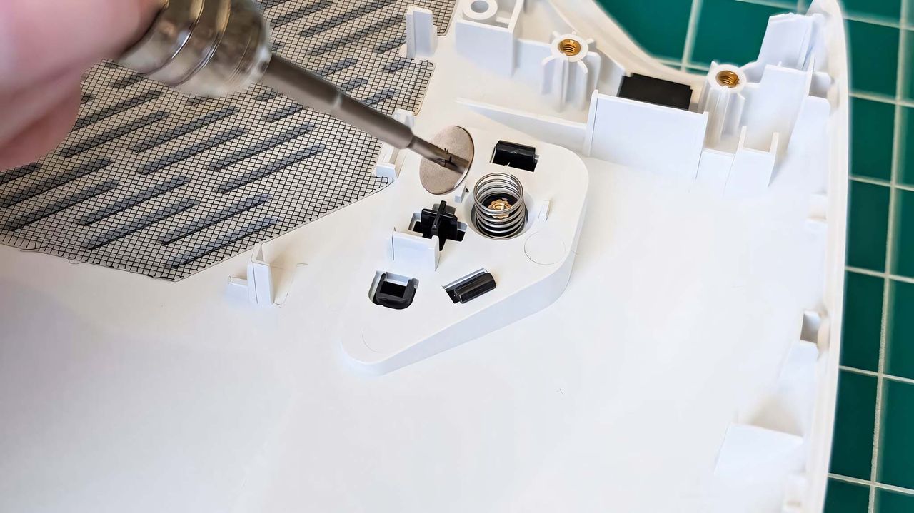 A screwdriver removing the back button screw on ROG Ally to show a spring underneath.