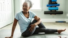 woman sitting on an exercise mat wearing leggings and tshirt in a seated twist facing the camera with her eyes closed. 