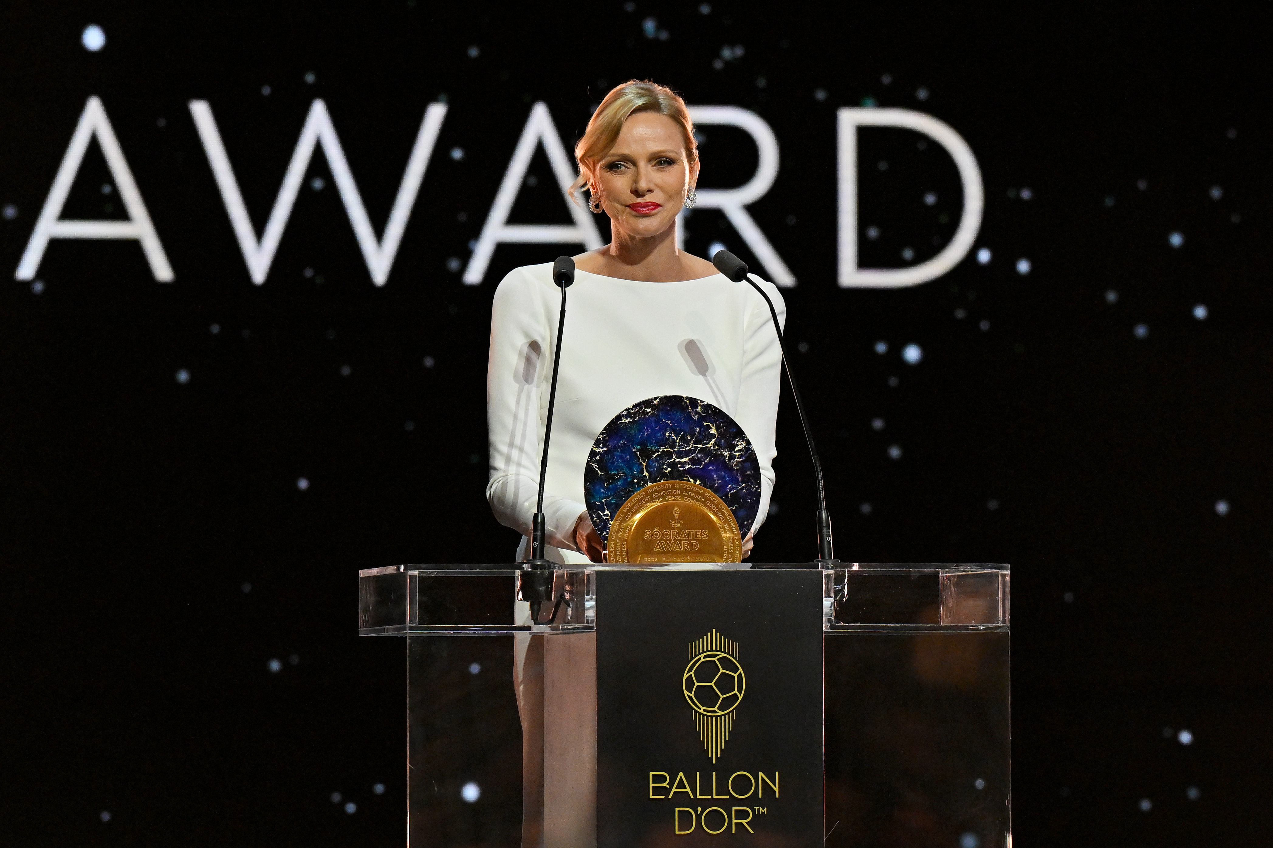 Princess Charlene wearing a white gown standing at a podium