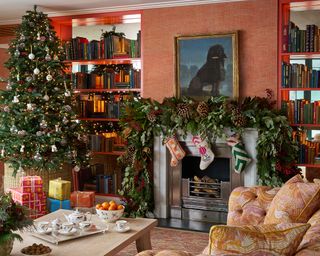 Colorful living room with fireplace decorated with foliage and stockings, large christmas tree with wrapped presents