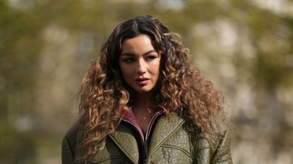 best straightener for curly hair - A woman with curly hair walking down the street wearing green oversized winter leather jacket with texture and burgundy lining 