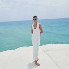 massimo dutti sale - woman wearing a white dress and sunglasses standing on a rock in front of the sea