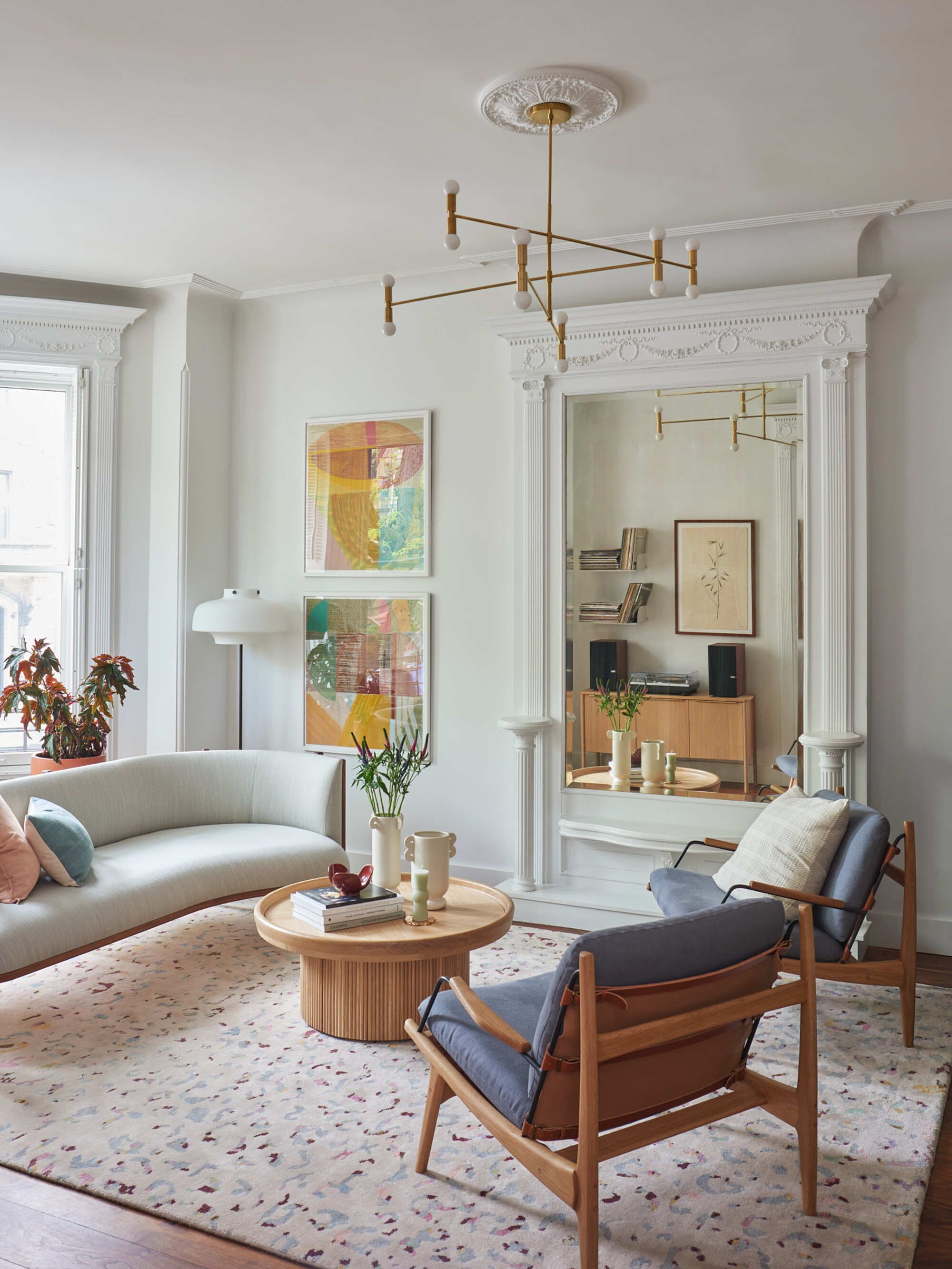 A white walled living room with pastel colored decor, a large terrazzo-style rug, and delicate crown molding