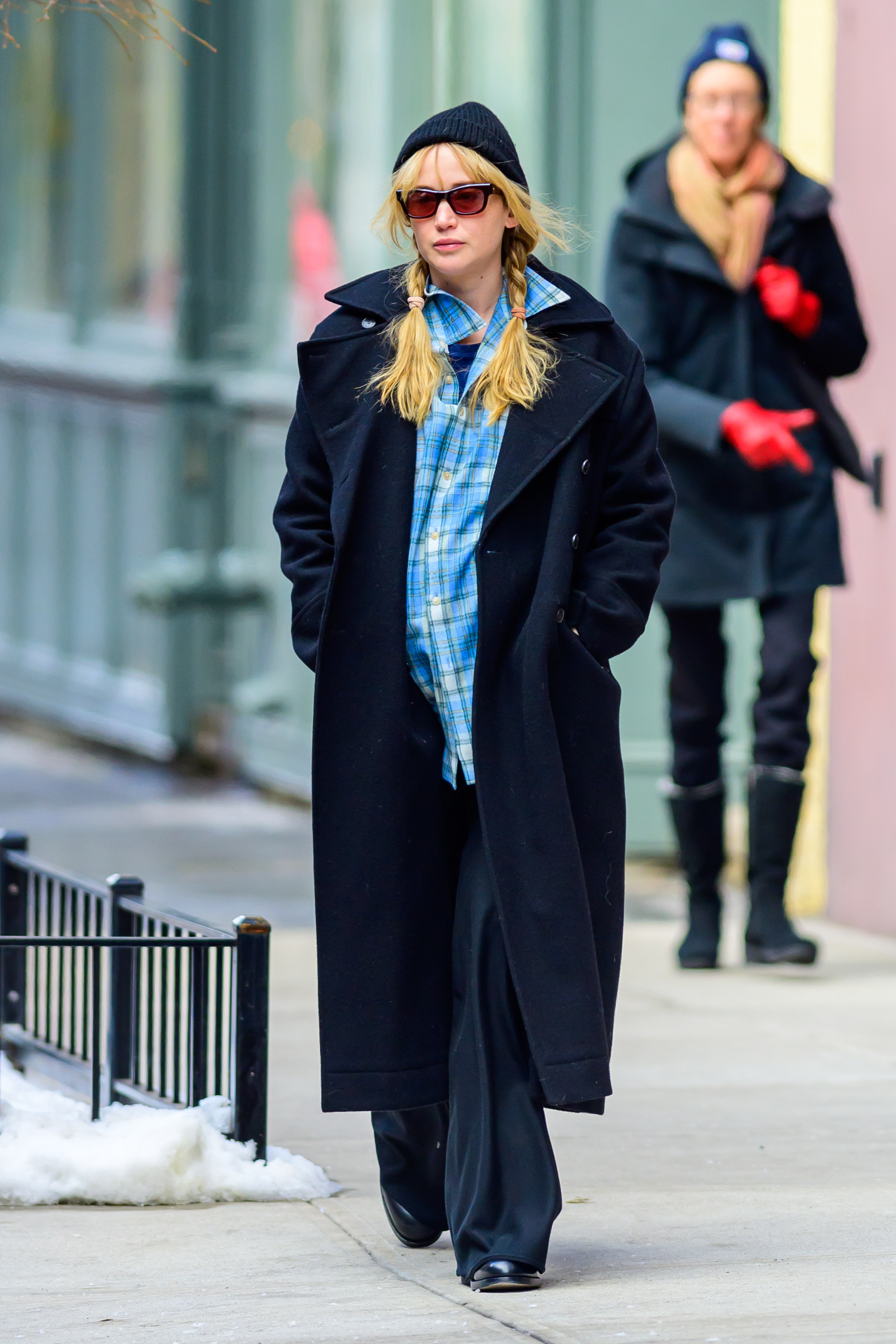 Jennifer Lawrence in New York City wearing a long navy-blue coat with black trousers, sunglasses, flat shoes, and a plaid shirt.