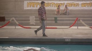 John Cusack in a red and white striped shirt walking along side a pool in The Sure Thing