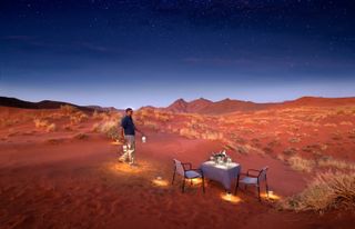 A man sets up a table for two in the middle of the Namib Desert outside of Sossusvlei Desert Lodge