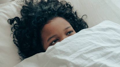 Woman under the covers with her eyes open, wellness tips, sleep hacks