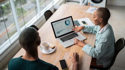 A financial planner shows a client a chart while sitting at his kitchen table.