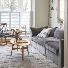 White painted living room with a grey sofa and a wooden coffee table on a rug in the middle of the room