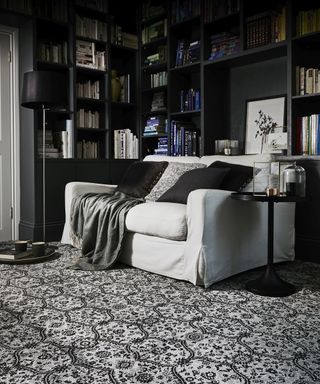 A dark living room with bookshelves, dark carpet decor and side table