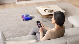 Woman on a couch controlling the Dyson 360 Vis Nav via a smartphone app
