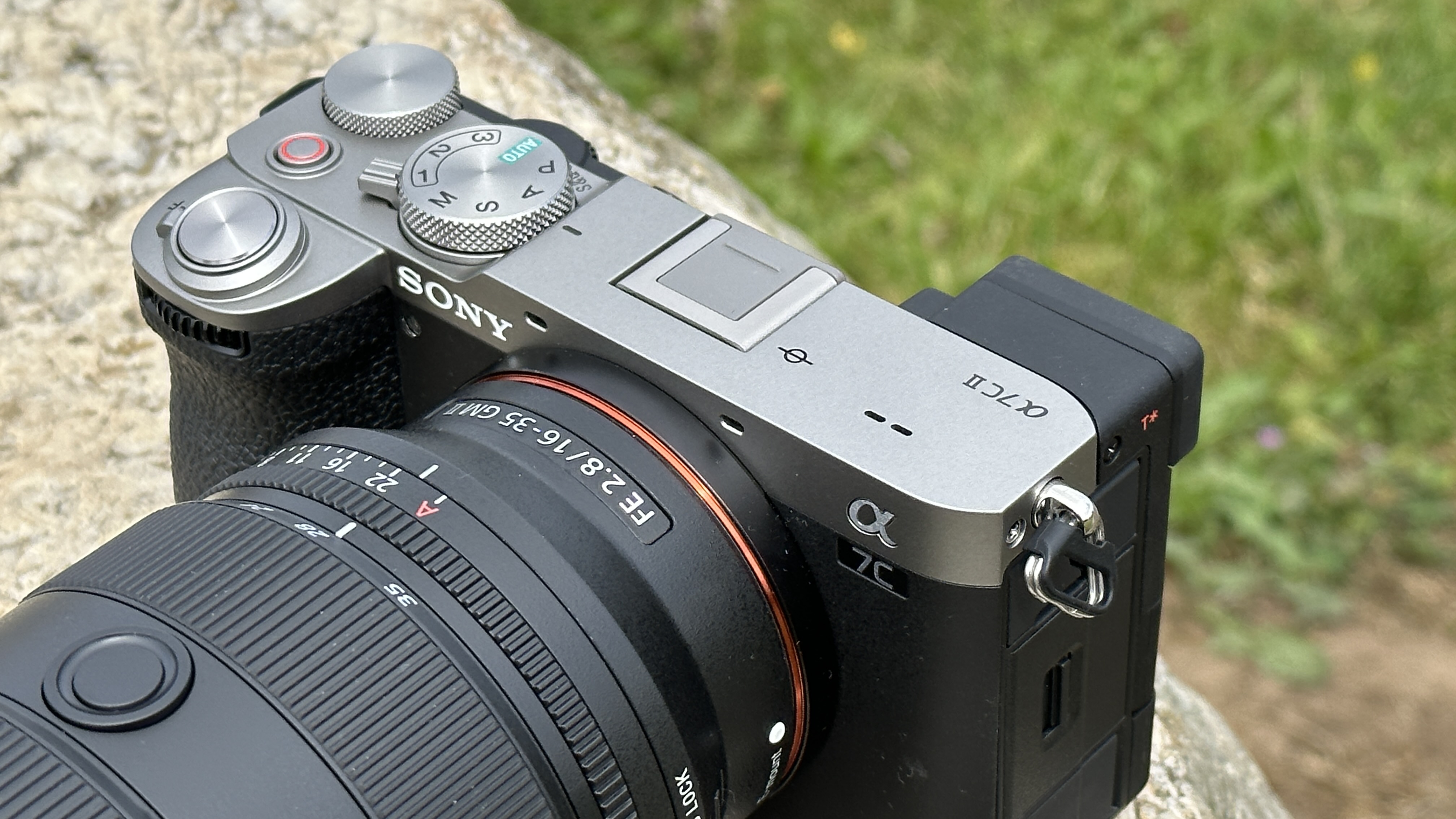 Close up of Sony A7C II mirrorless camera's top plate, outside on a rock with Sony FE 16-35mm F2.8 GM II lens attached