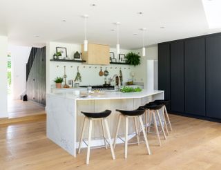 Marble effect kitchen island with high-backed seating in middle of wood floor