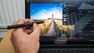 A hand using a stylus pen on the screen of an Asus ProArt PZ13 laptop on a wooden table