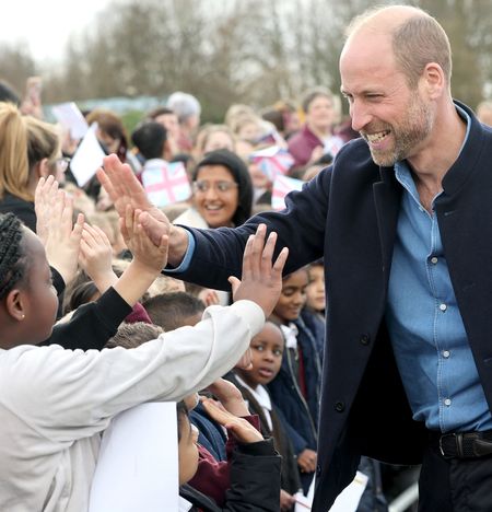 Prince William wearing a blue shirt and jacket giving a high five to a boy in a crowd of fans in March 2025