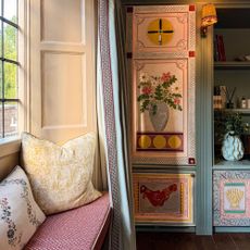 Upholstered window seat with two cushions beside built-in cabinetry painted with intricate designs
