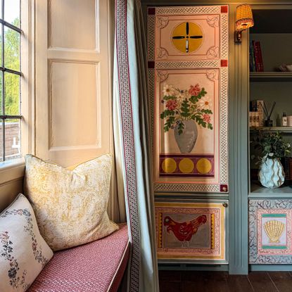 Upholstered window seat with two cushions beside built-in cabinetry painted with intricate designs