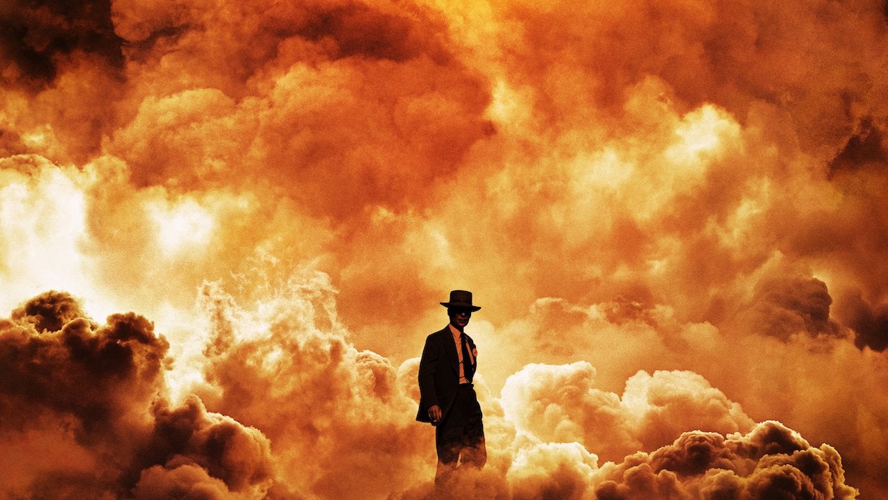 A promotional image for the Oppenheimer movie. Cillian Murphy (playing J. Robert Oppenheimer) stands in front of an explosion.