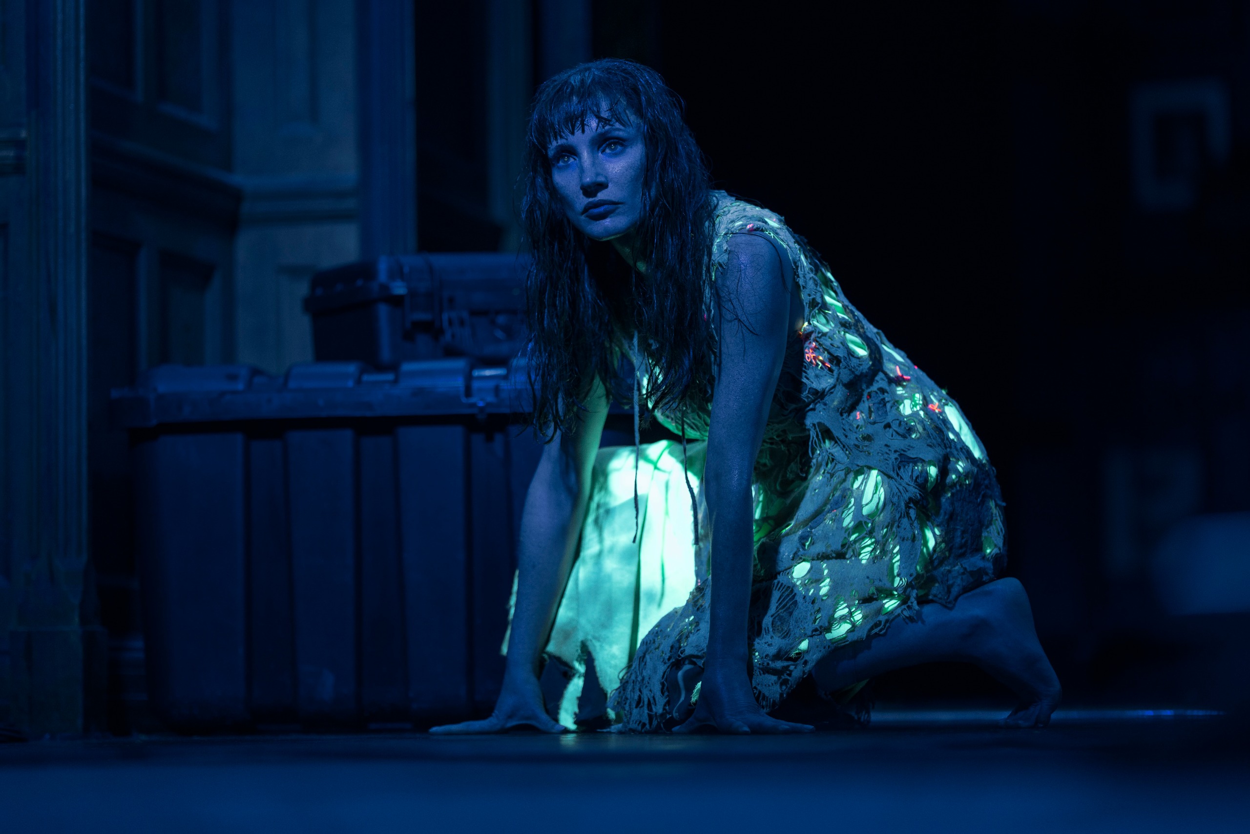 jessica chastain crawling on a floor wearing a dress lit up in green in a dark room in a scene from other mommy