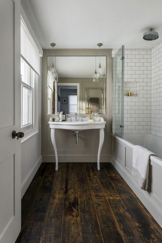 Bathroom with wooden flooring, white wall tiles, large basin and bath with shower over