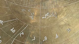 close-up view of a bronze astronomical instrument, showing arabic and hebrew markings.