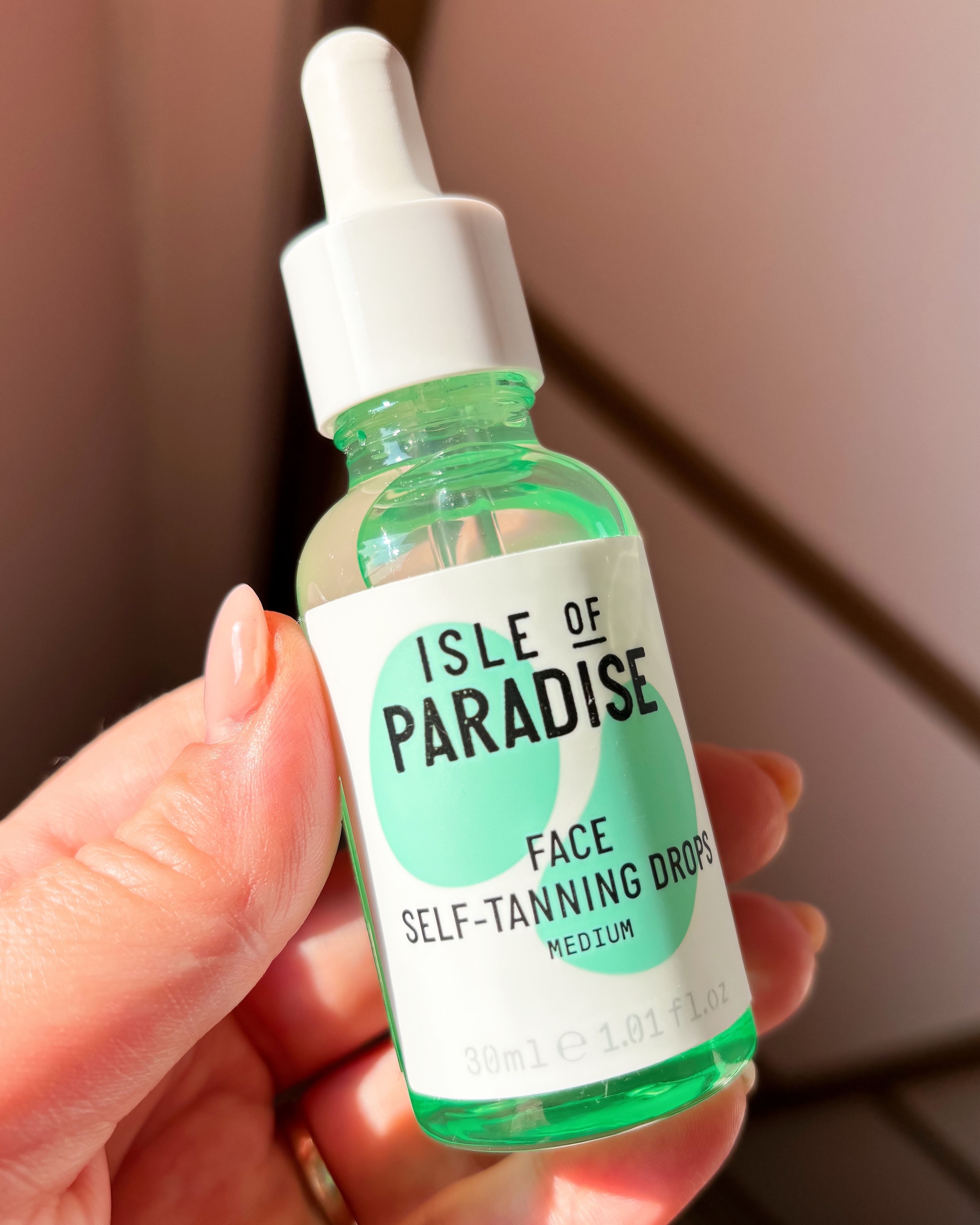 A woman holds a bottle of Isle of Paradise Face Tanning Drops