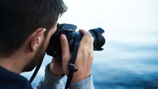 Best DSLR camera: Image shows man using DSLR next to lake