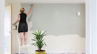 A woman paints a wall sage green