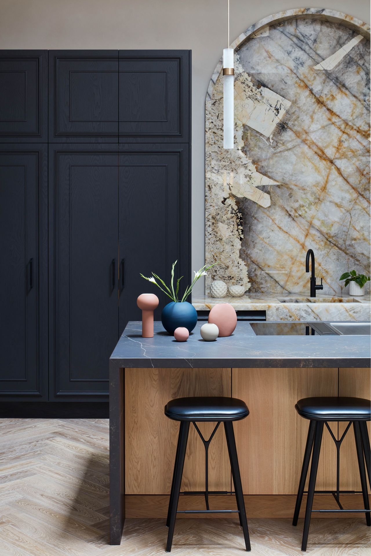 a large, arched onyx stone backsplash in a kitchen above the sink and in front of the kitchen island with black stool seating and tall black cabinetry