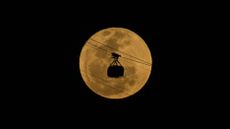 The silhouette of a cable car passes in front of the moon