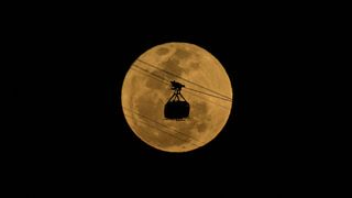 The silhouette of a cable car passes in front of the moon