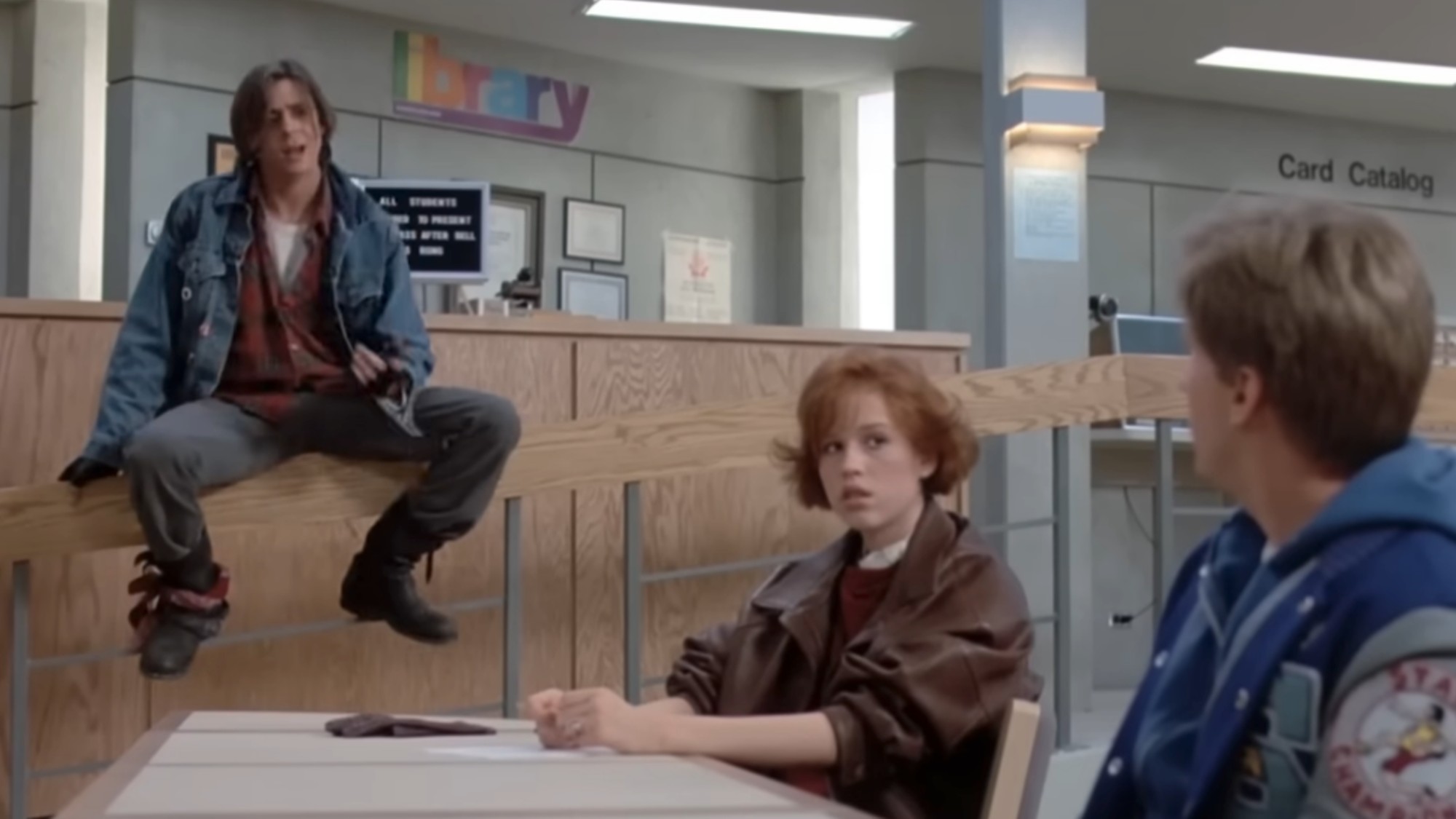 Judd Nelson in the background, sitting on a railing with Molly Ringwald sitting at a table in front of him. Emilio Estevez is facing away from the camera next to Ringwald in The Breakfast Club.