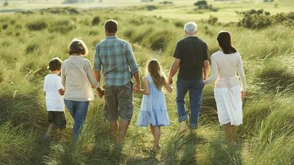 Multiple generations of a family hold hands and walk through a field.